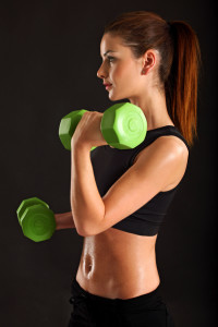 Photo of a slim female lifting dumbbells doing bicep curls over black background